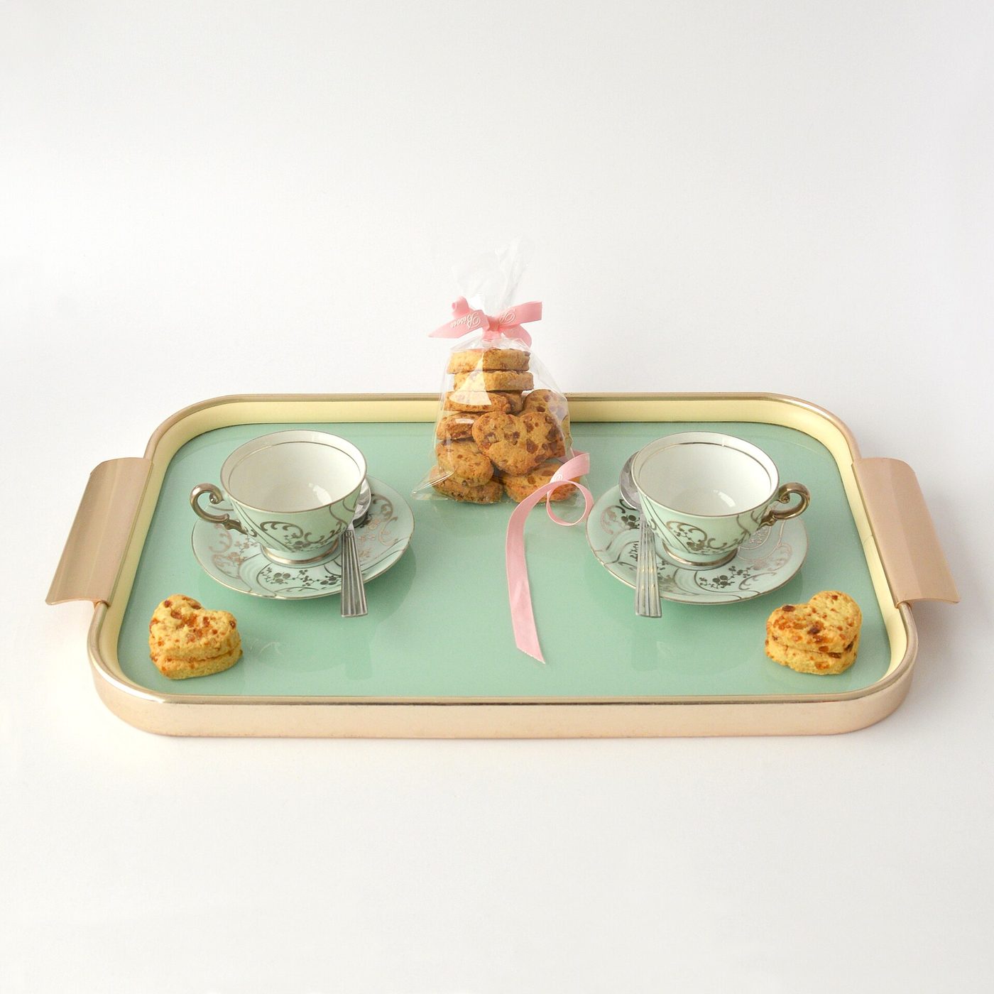 A mint-green tray set with two china teacups and small biscuits, for afternoon tea.