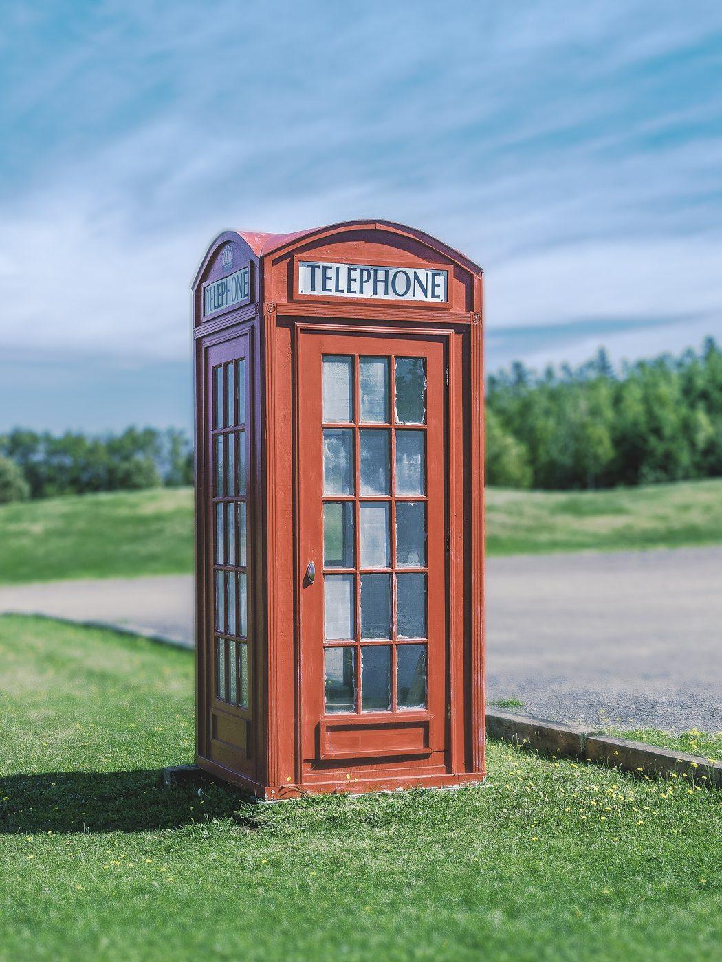 A traditional red telephone box standing on a grass verge beside a road.